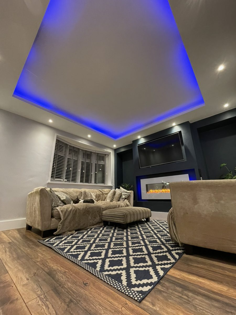 The same living room with an LED-lit suspended ceiling and a built-in media wall