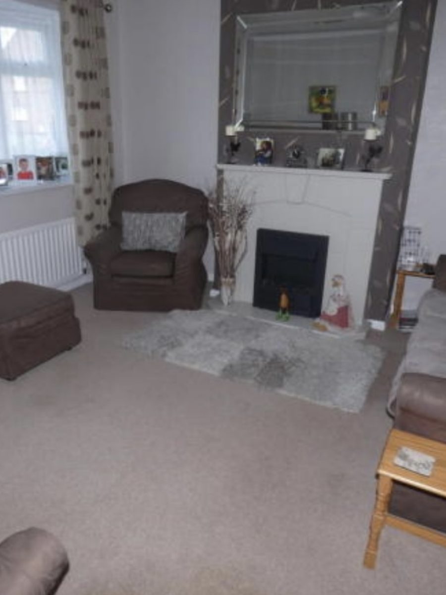 Dated living room with a fire surround and papered chimney breast before renovation